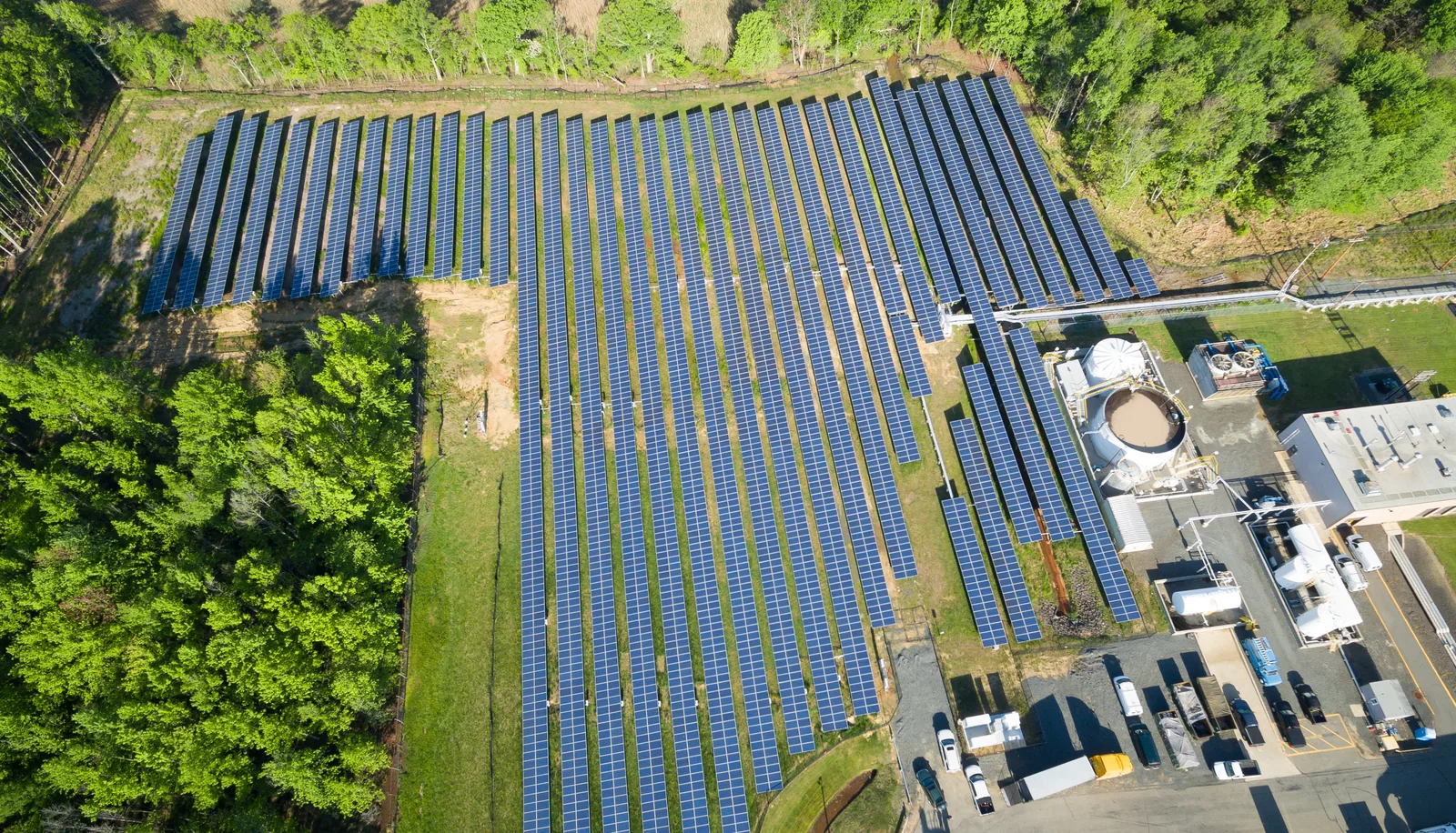 Ground-mounted solar array photographed from altitude, rows and inverter pads visible