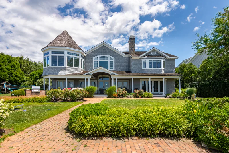 Shingle-style estate photographed from low aerial angle, lawn and gardens in foreground